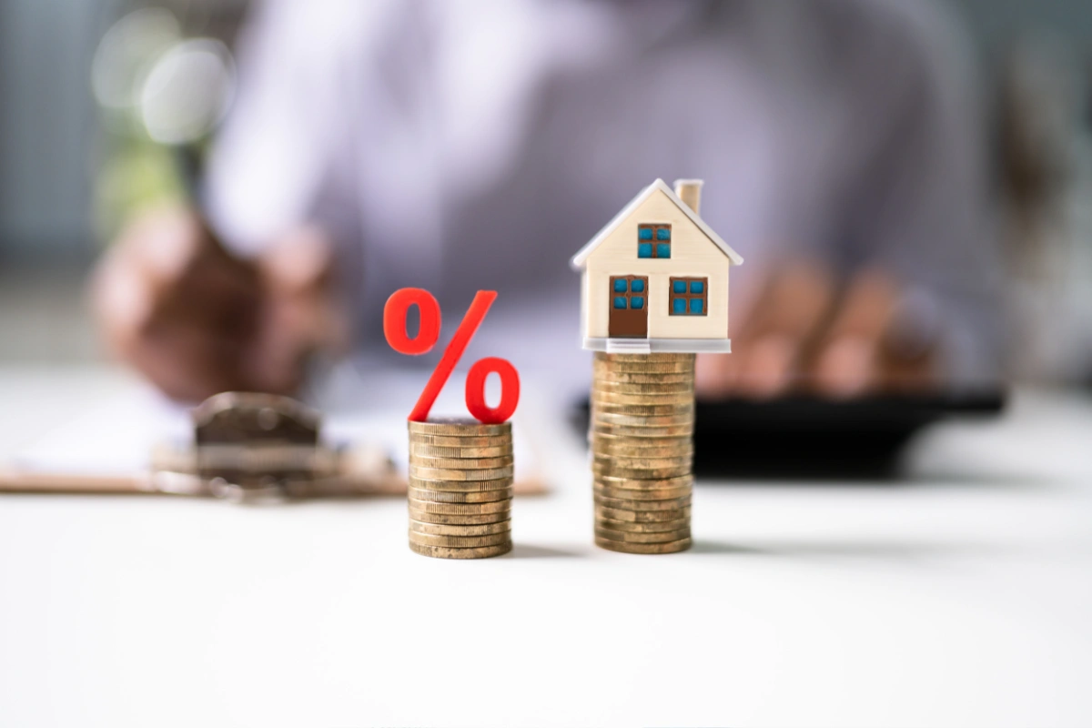 Mini house model on stacked coins beside red percent symbol representing changing mortgage interest rates and home affordability